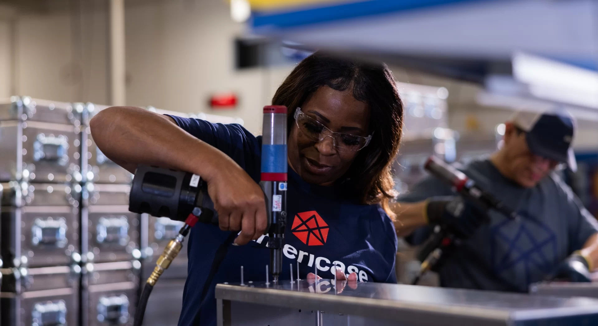 Photo of female Americase employee wearing Amricase apparel and safety glasses drilling a custom case together in the shop.