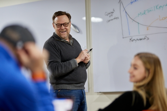 Photo of SEO/PPC/Digital Marketing, Rod Holmes, Laughing with fellow co-workers in a meeting while he's standing at a white board with a marker in his hand.