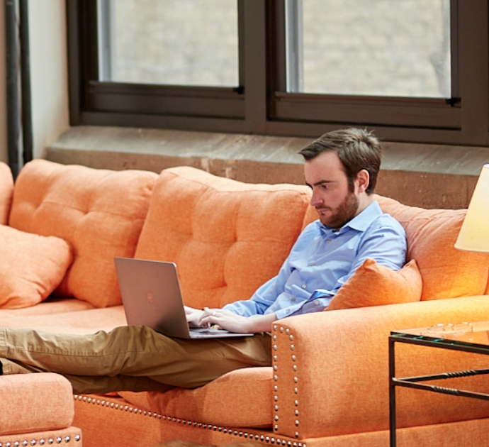 MonogramGroup Hero Photo of Account Executive, Michael Calk working on his laptop comfortably on the office couch.