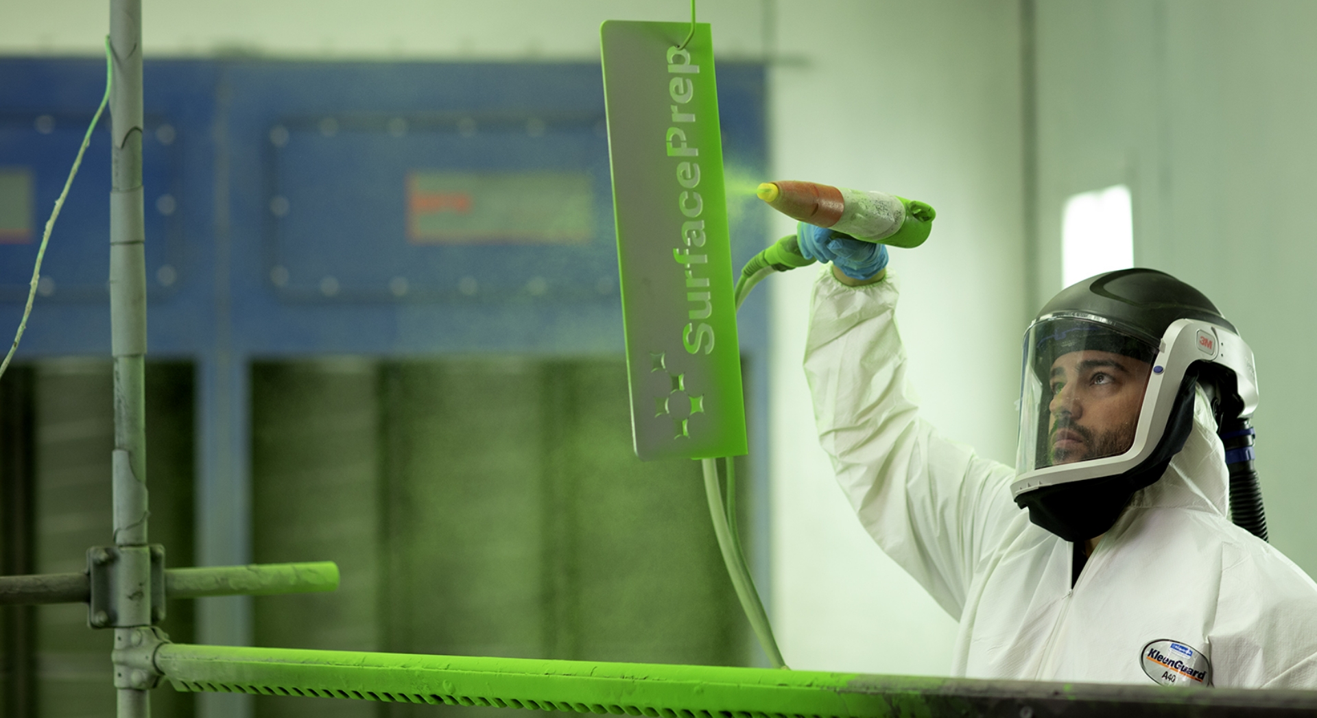 SurfacePrep Hero Photo; man in full safety suit spray painting a piece of metal with the the SurfacePrep emblem green.