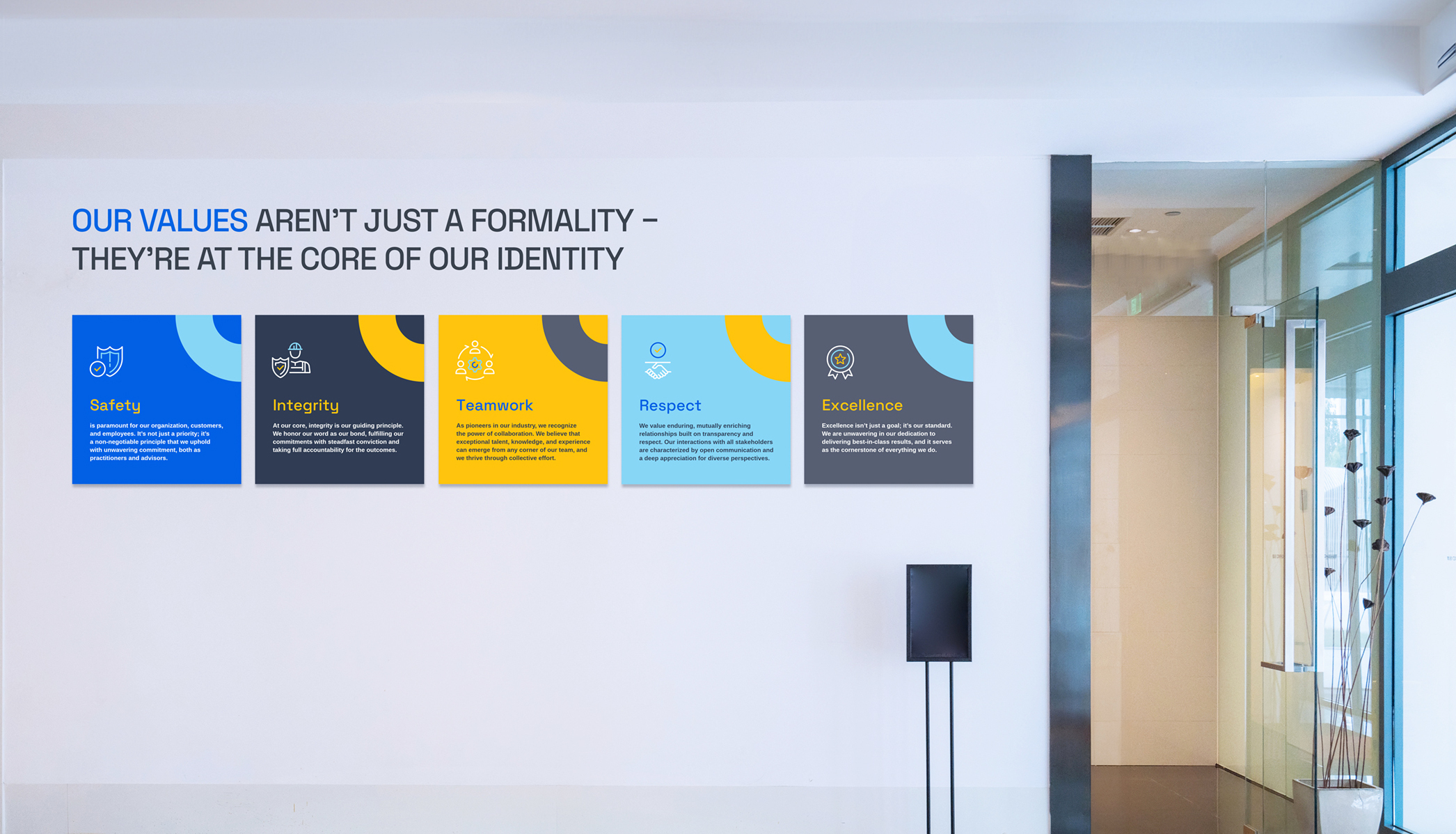 Wall with a sign that reads OUR VALUES ARENT JUST A FORMALITY – THEYRE AT THE CORE OF OUR IDENTITY alongside five colorful panels representing values: Safety, Integrity, Teamwork, Respect, and Excellence. Minimalist office decor visible on the right.