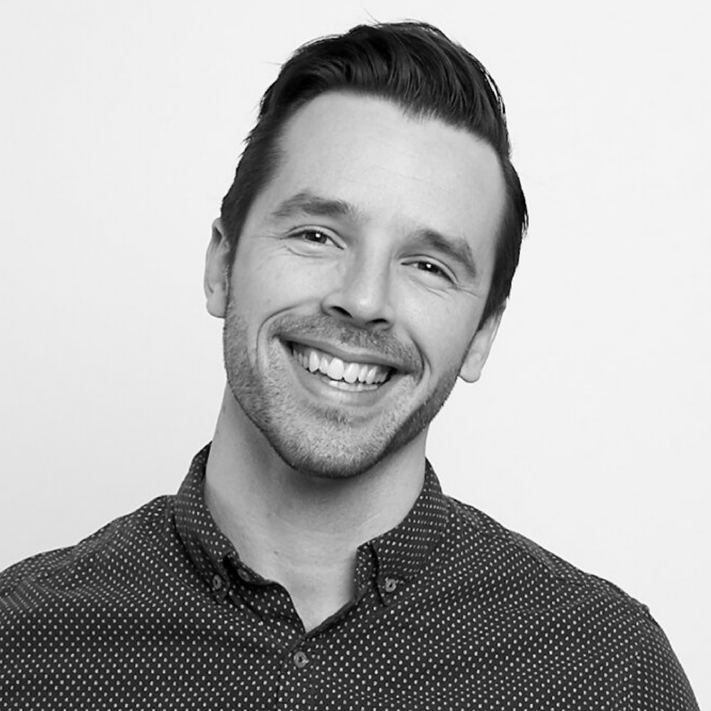 Smiling man with short, dark hair in a button-up shirt. The image is black and white.